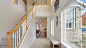 A spacious hallway with a wooden staircase, a bench, and a large window with a view of the outside.