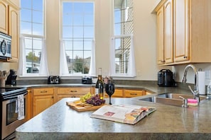 Una cocina con armarios de madera, encimera de granito, una botella de vino, una copa de vino, tabla de cortar con frutas y un libro de cocina.