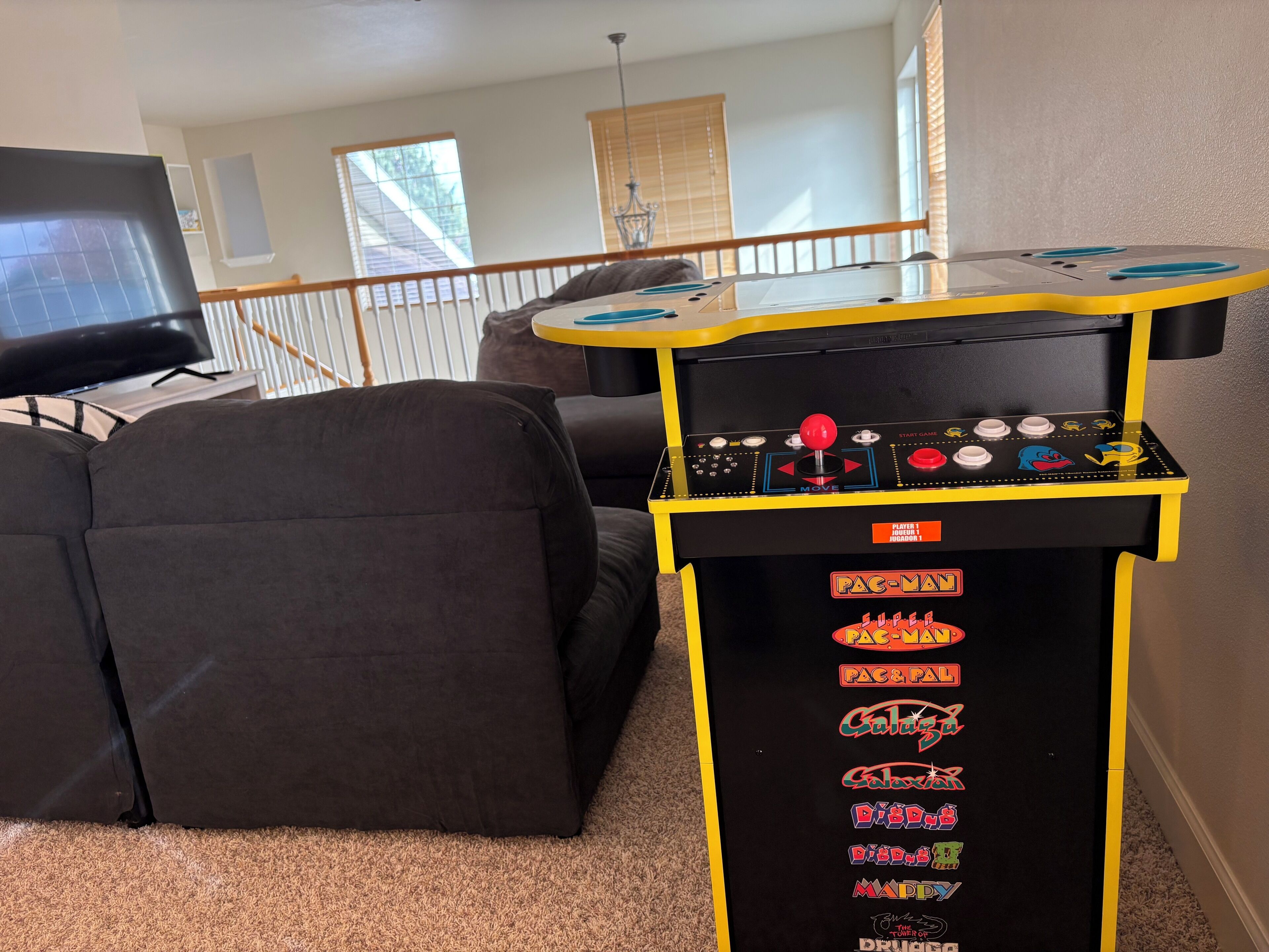 Ein Zimmer mit einem Spieltisch, der Arcade-Spiele, einer Couch und einem Fernseher bietet.