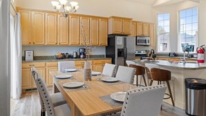 A modern kitchen with wooden cabinets, a dining table set for four, and a large island with a sink.
