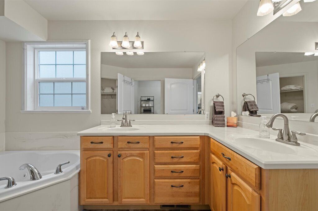 A modern bathroom with a freestanding bathtub, a double sink vanity, wooden cabinetry, and a large mirror.
