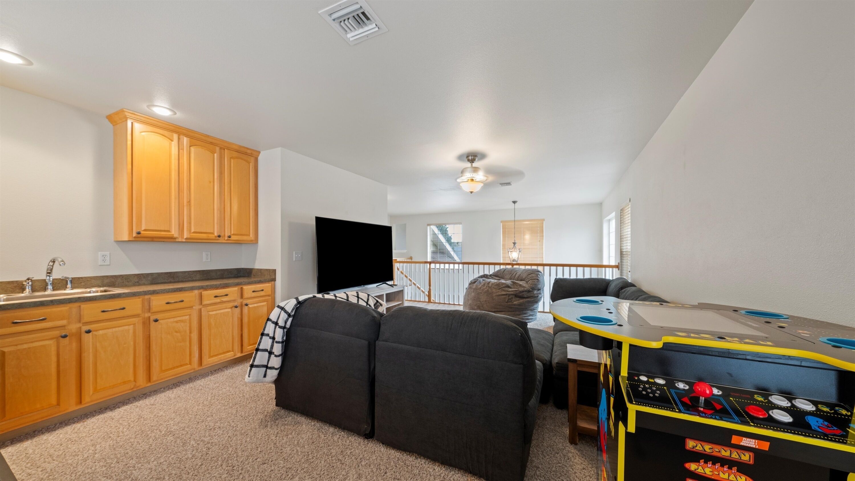 A compact living space with a kitchenette, a flat-screen TV, a bean bag chair, a gaming table, and a staircase leading to an upper level.