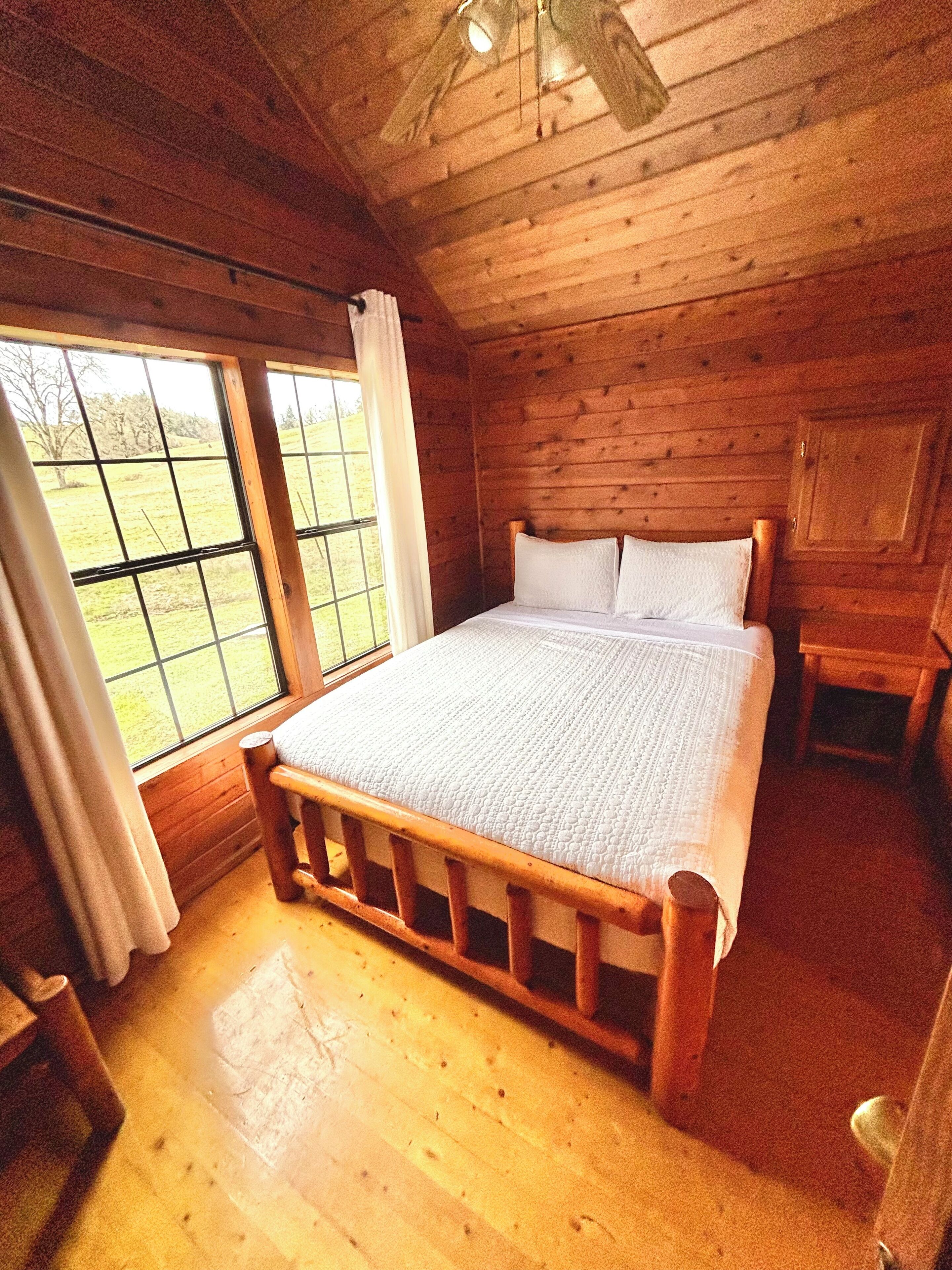 A wooden cabin bedroom with a bed, a window, and a wooden ceiling.