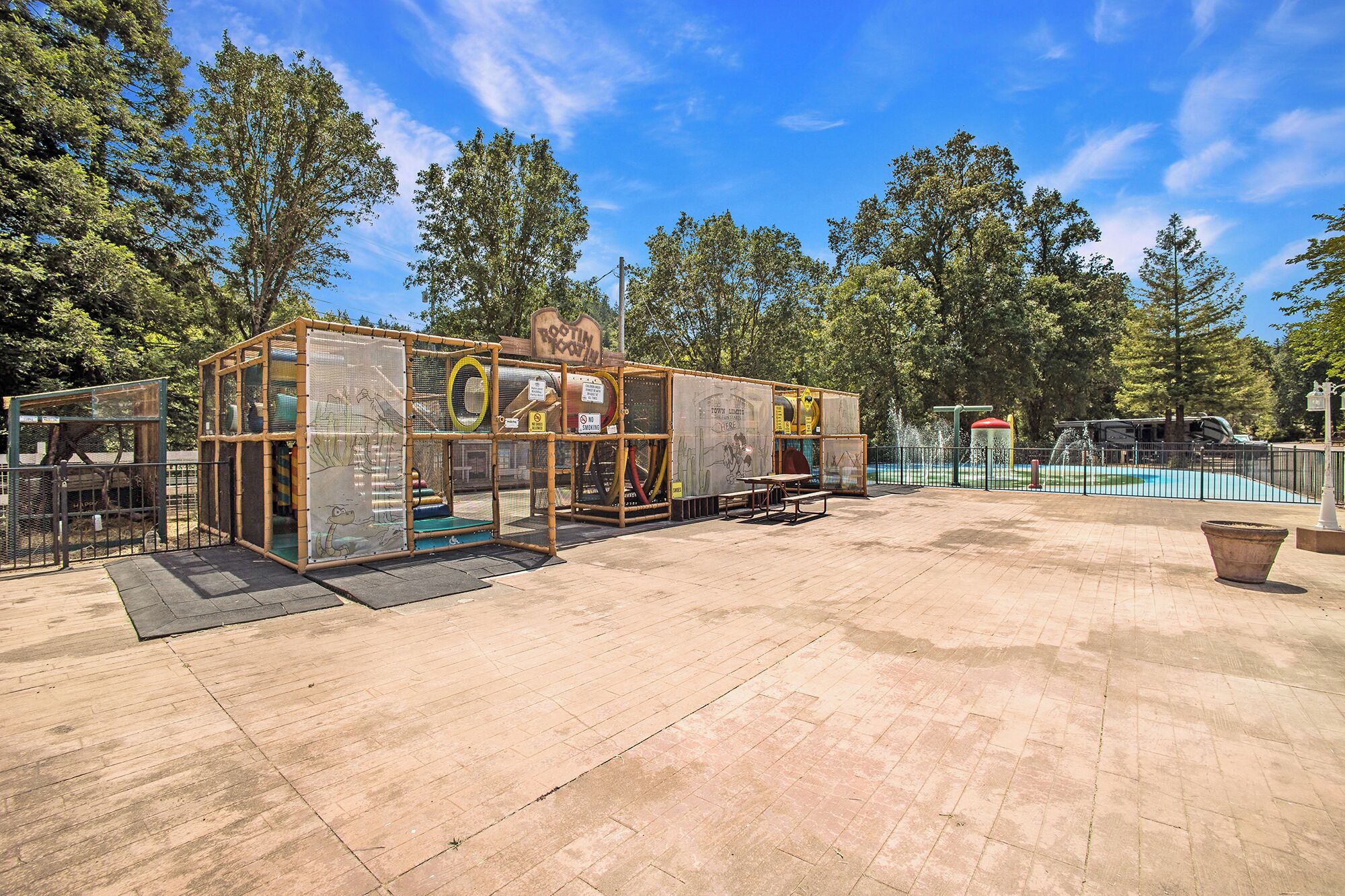 Een speeltuin met een omheind speelgedeelte, picknicktafels en een zwembad.