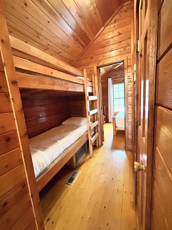 Ein Holzblockhaus-Innenraum mit Etagenbetten, Holzboden und einer Tür zu einem anderen Raum.