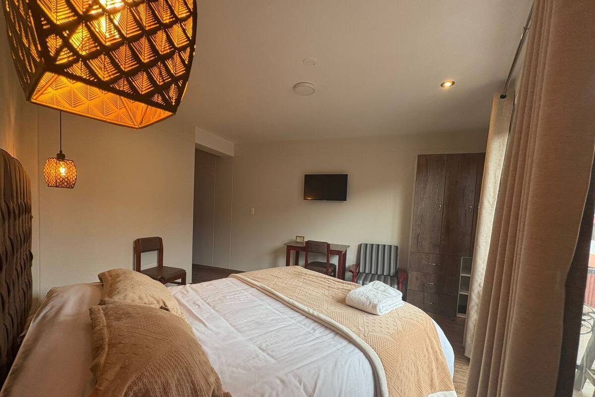 A hotel room with a large bed, a television on the wall, and a seating area with chairs.