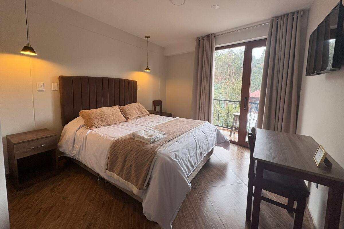 A bedroom with a bed, bedside tables, a desk, and a TV on the wall.
