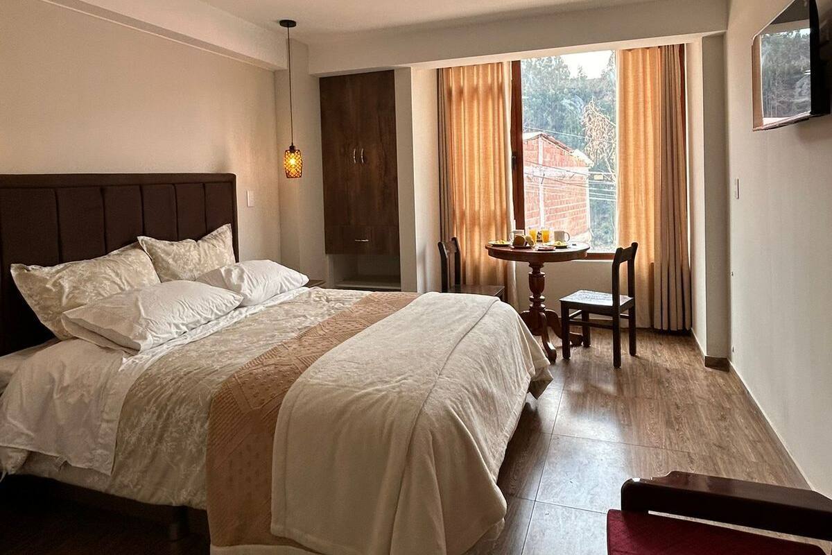 A hotel room with a large bed, a desk with a chair, and a window with curtains.