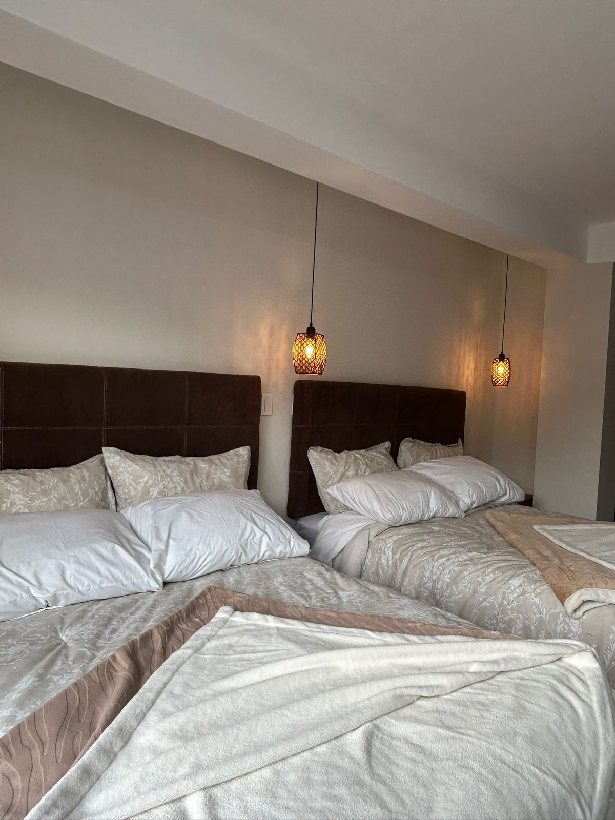 A hotel room with two beds, a dark headboard, and two hanging pendant lights.