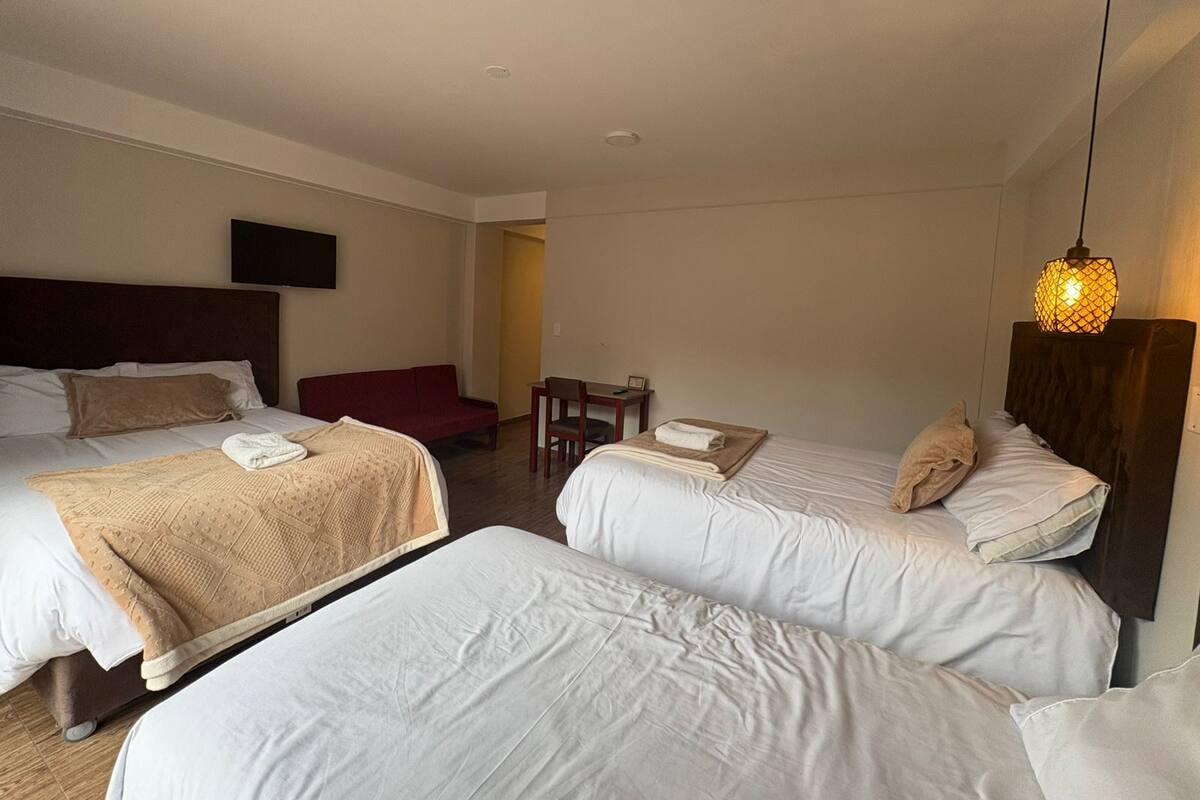 A hotel room with two beds, a red sofa, a small table, and a TV mounted on the wall.