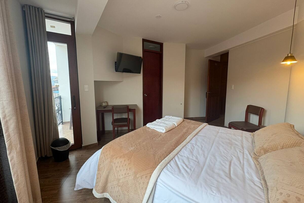 A hotel room with a bed, a desk, a chair, a television, and a balcony view.