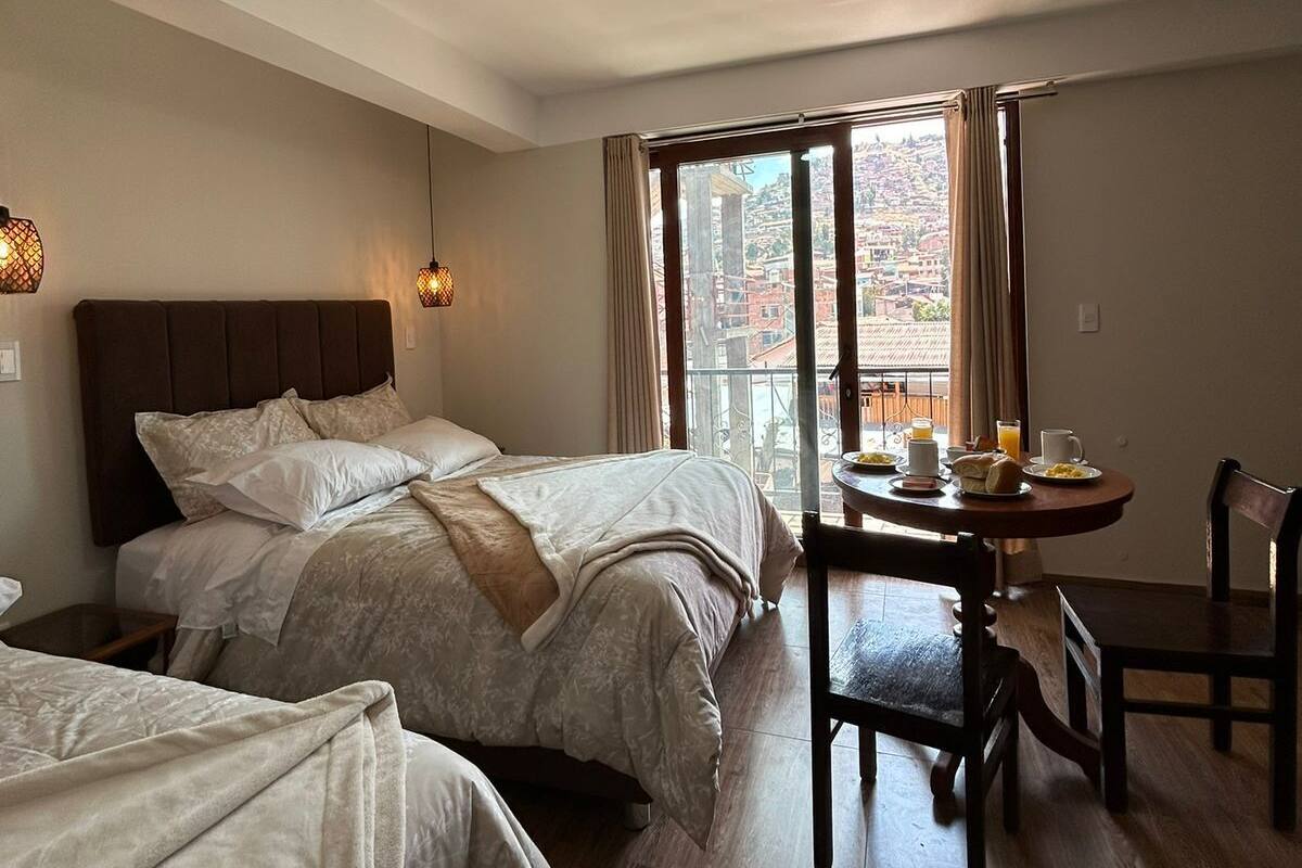A hotel room with two beds, a dining table with breakfast, and a view of the city.