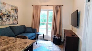 Ein Wohnzimmer mit einer Couch, einem kleinen Tisch, einem Fernseher und einem Fenster mit Vorhängen.