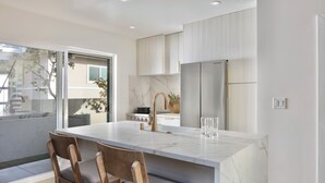 A modern kitchen with a marble island, wooden chairs, and stainless steel appliances. - The Modern Kailua Beach House (Kailua)
