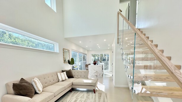 A modern living room with a sectional sofa, a glass staircase, and a view of the outdoors. - The Modern Kailua Beach House (Kailua)