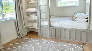 A room with a bunk bed, a window with curtains, a shelf with folded towels, and a geometric rug. - The Modern Kailua Beach House (Kailua)