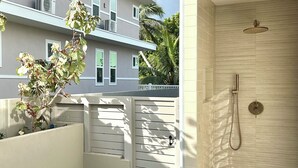 A modern outdoor shower with a tiled wall, a small grassy area, and a white fence. - The Modern Kailua Beach House (Kailua)