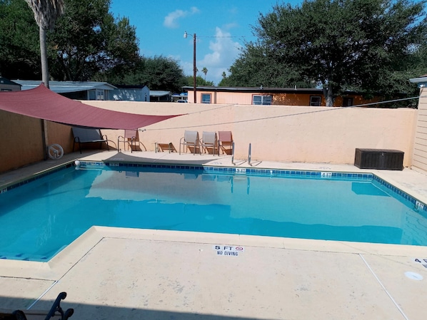 Una piscina rectangular con un cartel de prohibición de saltos, rodeada por un muro color beige y cubierta por un toldo rojo.