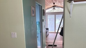Ein Flur, der zu einem Zimmer mit Deckenventilator, Tür und Fenster führt.