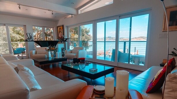 A modern living room with a white sofa, a glass coffee table, and a view of the sea through large windows. - Eria events and stay on Paradise, premier modern waterfront retreat (Corte Madera)