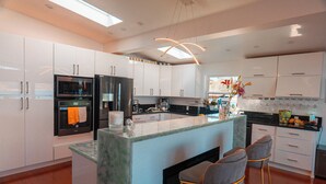 A modern kitchen with white cabinets, a central island with bar stools, and a large window providing natural light. - Eria events and stay on Paradise, premier modern waterfront retreat (Corte Madera)