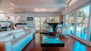 A modern living room with a white sofa, a coffee table, and a view of the outdoors through large windows. - Eria events and stay on Paradise, premier modern waterfront retreat (Corte Madera)