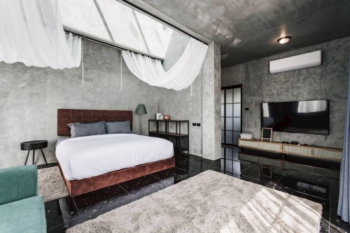 Une chambre à coucher moderne avec un grand lit, un téléviseur fixé au mur et un décor minimaliste.