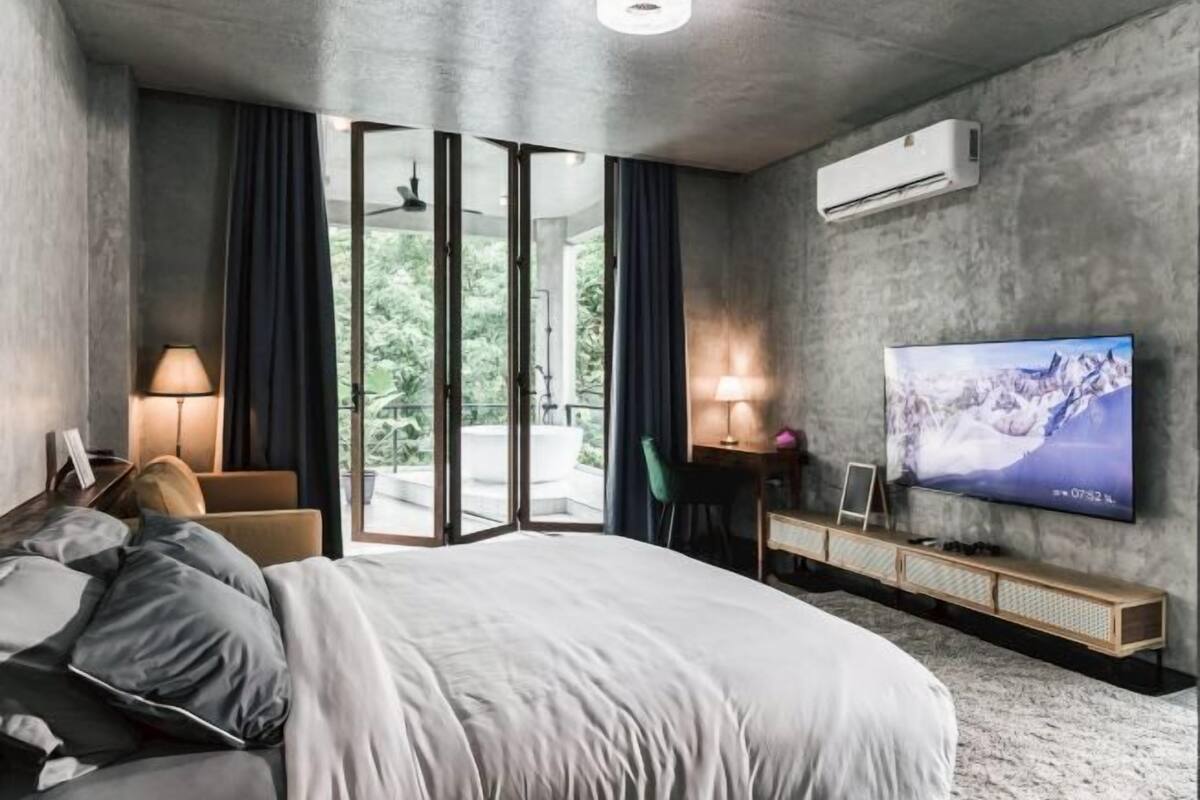 Une chambre d’hôtel moderne avec un grand lit, un téléviseur fixé au mur et un balcon agrémenté de rideaux.
