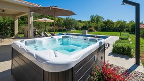Een hottub met een pergola en parasol, omringd door een zwembad en tuin.