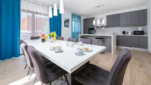 Een moderne eethoek met een witte tafel, donkere stoelen en een keuken op de achtergrond.