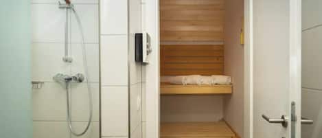 Un baño pequeño y funcional con ducha, estante de madera y puerta.