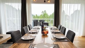 A dining room with a long table set for six, a fruit bowl, and a bottle of wine.