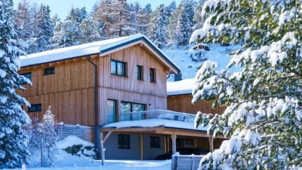 A wooden cabin with a balcony, surrounded by snow-covered trees.