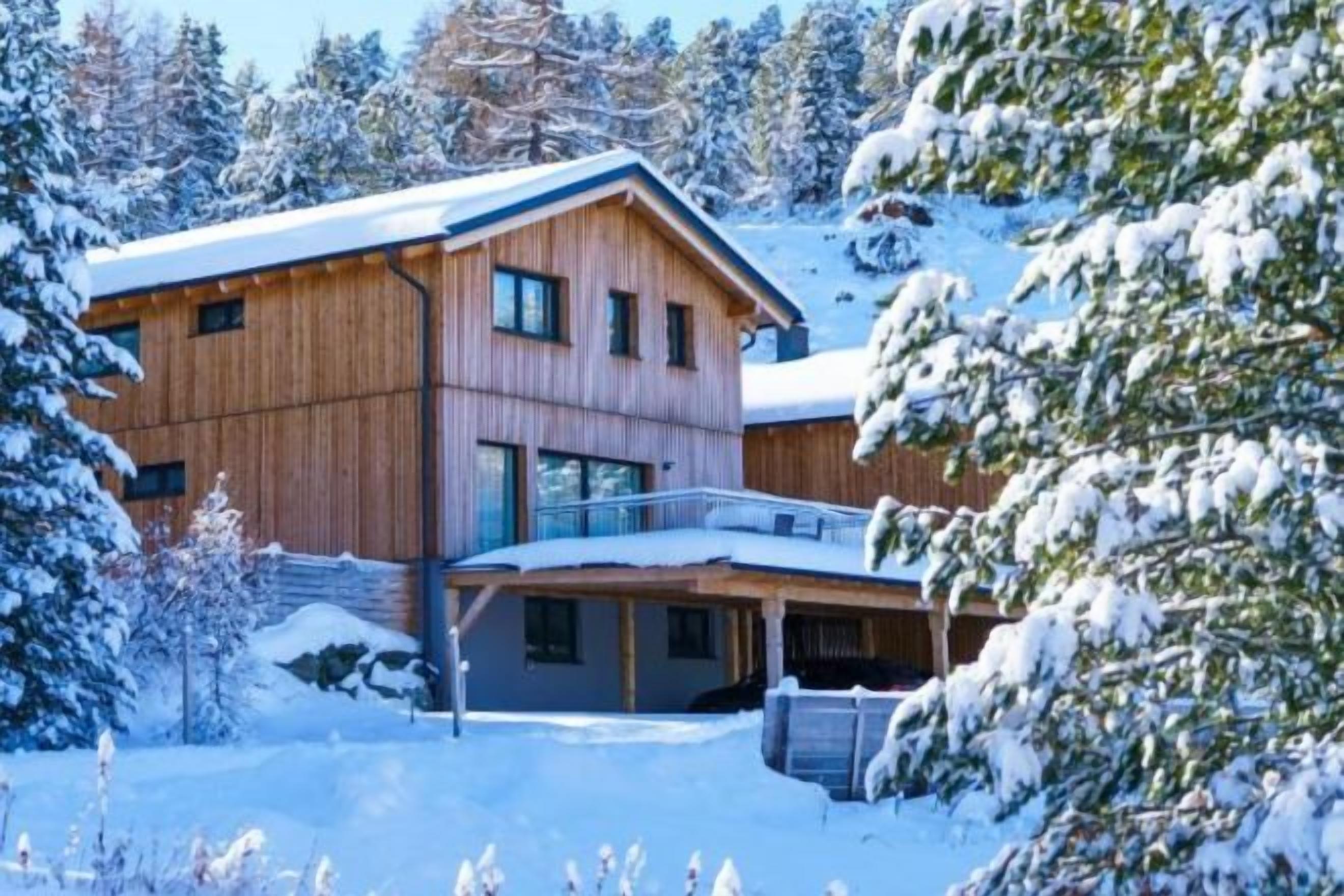 A wooden chalet with a balcony, surrounded by snow-covered trees.