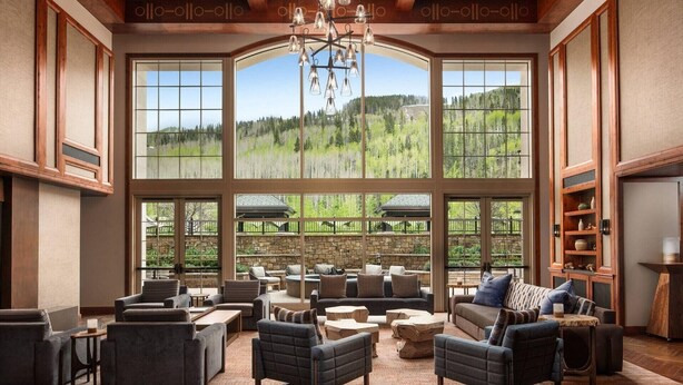 Un vaste espace salon doté de grandes fenêtres offrant une vue sur un paysage boisé. Le mobilier comprend des canapés, des fauteuils et une table basse.