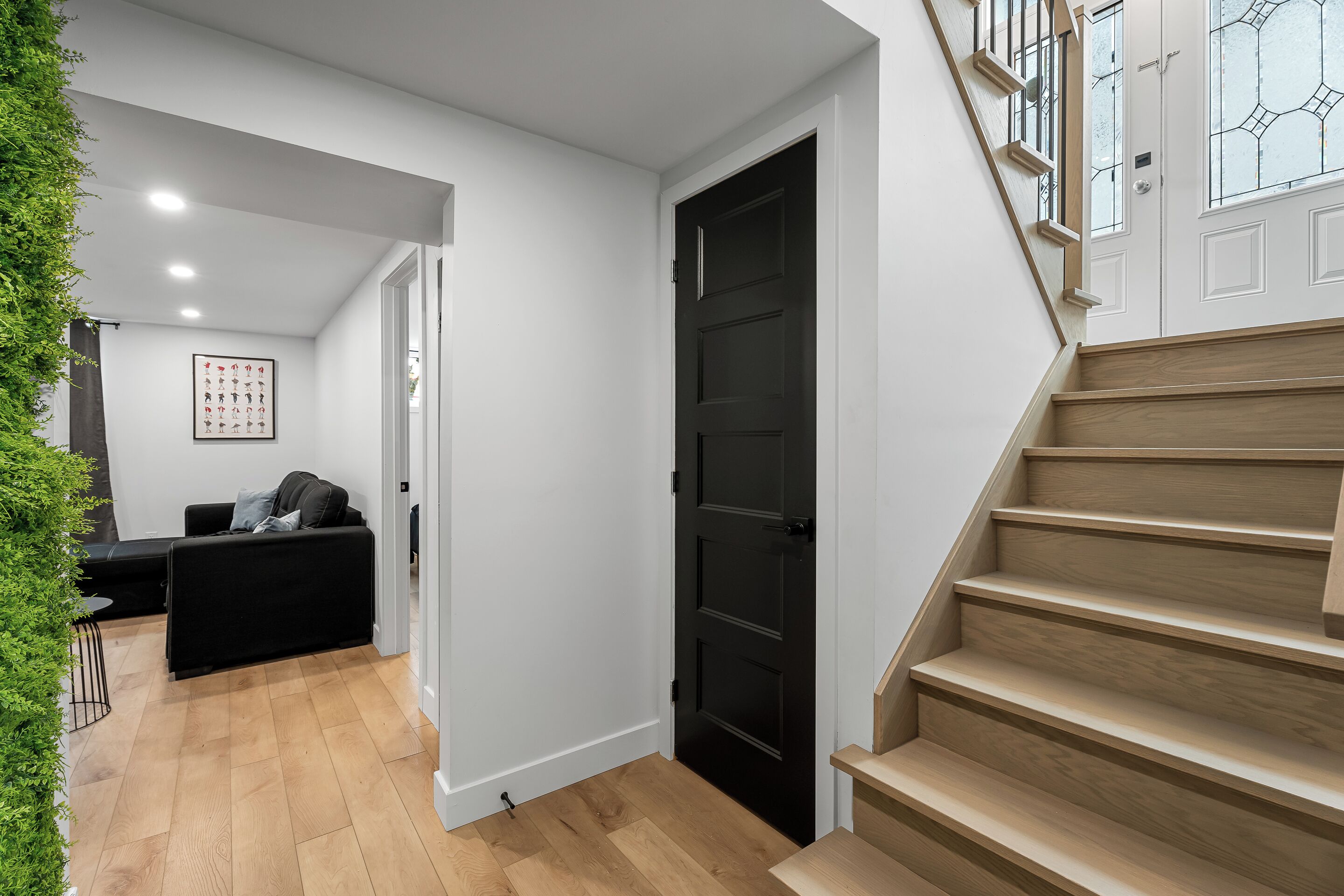 Un interior moderno con una escalera, una puerta negra y una zona de estar con un sofá y un cuadro enmarcado.