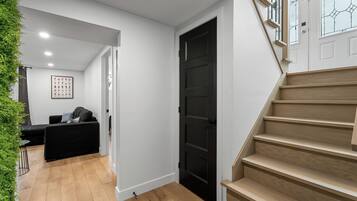 Un interior moderno con una escalera, una puerta negra y una zona de estar con un sofá y un cuadro enmarcado.