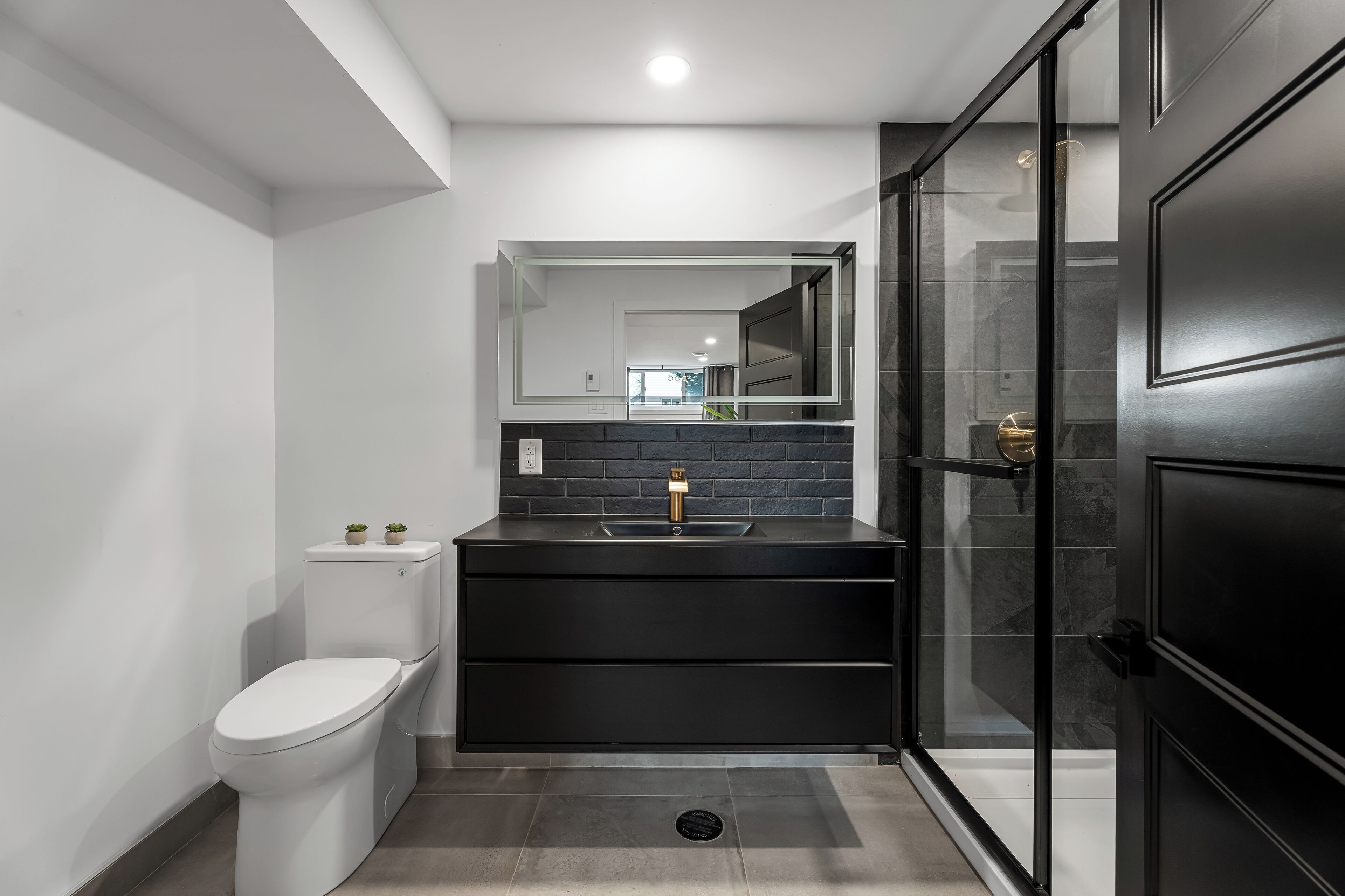 Une salle de bain moderne avec des toilettes, un lavabo noir et une douche à parois de verre.