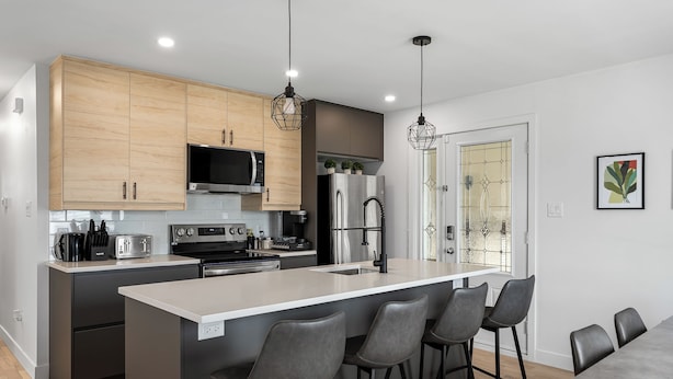 A modern kitchen with wooden cabinets, stainless steel appliances, a central island with bar stools, and pendant lighting. - 4-bedroom house in delightful Longueuil with AC, bar and karaoke (Longueuil)