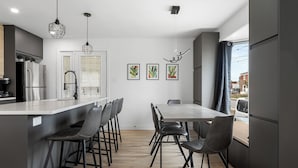 A modern kitchen with a central island, bar stools, and a dining table with chairs. - 4-bedroom house in delightful Longueuil with AC, bar and karaoke (Longueuil)