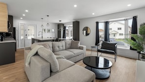 A modern living room with a sectional sofa, a round coffee table, and a dining area. - 4-bedroom house in delightful Longueuil with AC, bar and karaoke (Longueuil)