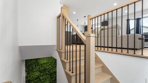 A modern staircase with wooden steps and black railings, leading to a living area with a green wall and a sofa. - 4-bedroom house in delightful Longueuil with AC, bar and karaoke (Longueuil)
