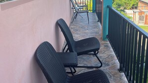Un balcon avec deux fauteuils en osier noir, un sol carrelé en pierre et une vue sur le clocher d’une église et l’océan.