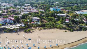 Vista aerea di una zona costiera con spiaggia, edifici e una grande freccia verde che indica un punto specifico.