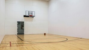 Un terrain de basket avec un panier, un plancher en bois et des murs blancs.