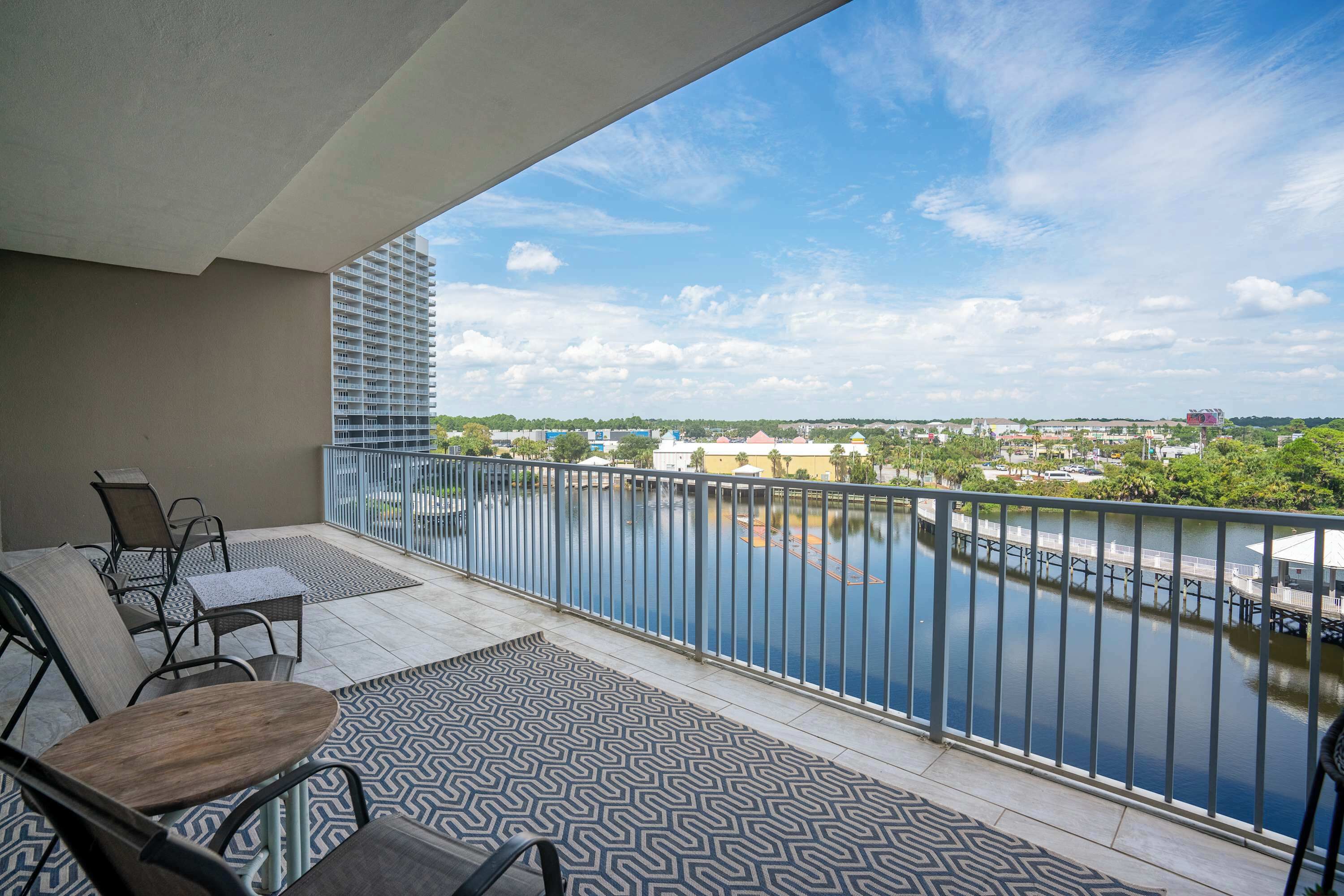 A balcony with a view of a river, outdoor furniture, and a patterned rug.