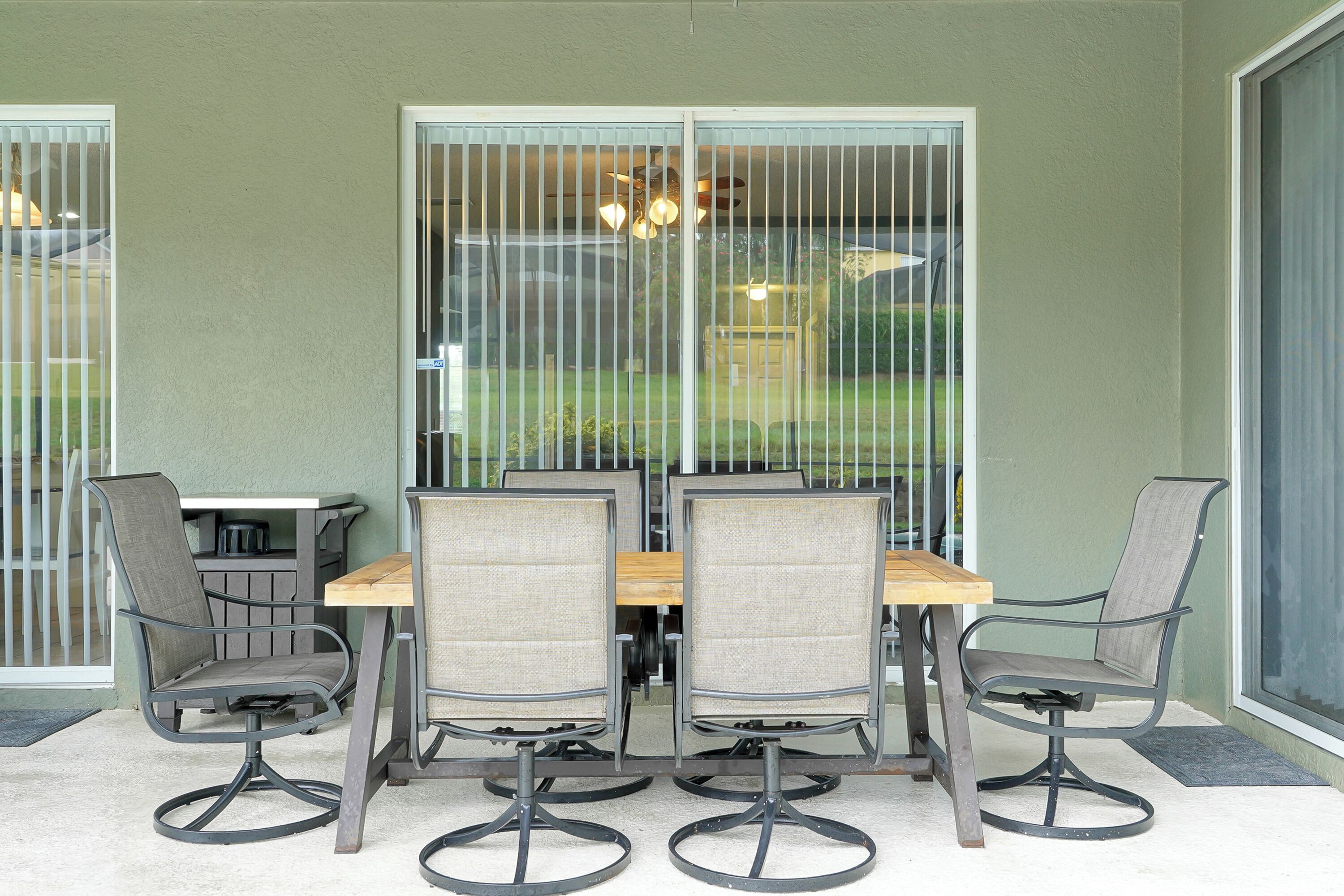 A patio with a table and four chairs, a sliding glass door, and a view of a lawn and car.