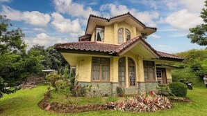 Una casa de dos pisos con techo de tejas, base de piedra y un jardín bien cuidado.
