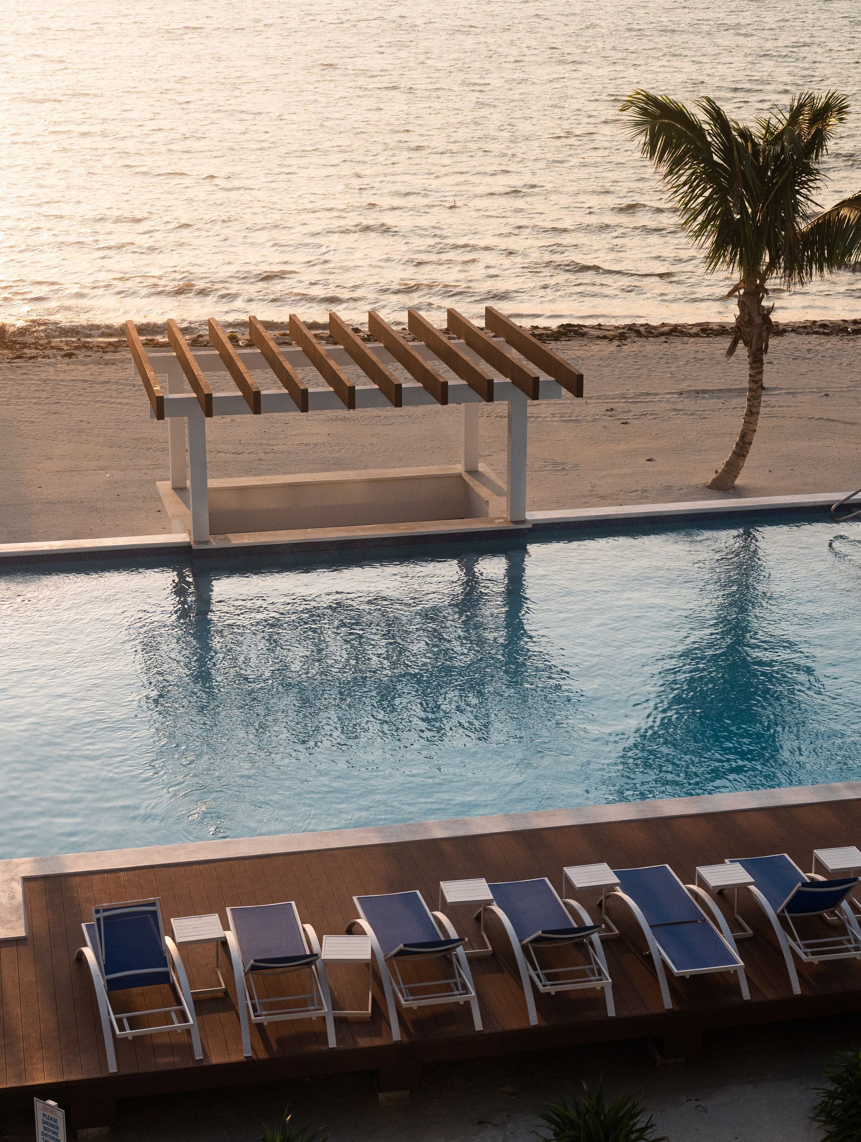 A poolside area with lounge chairs and a pergola overlooking the sea.