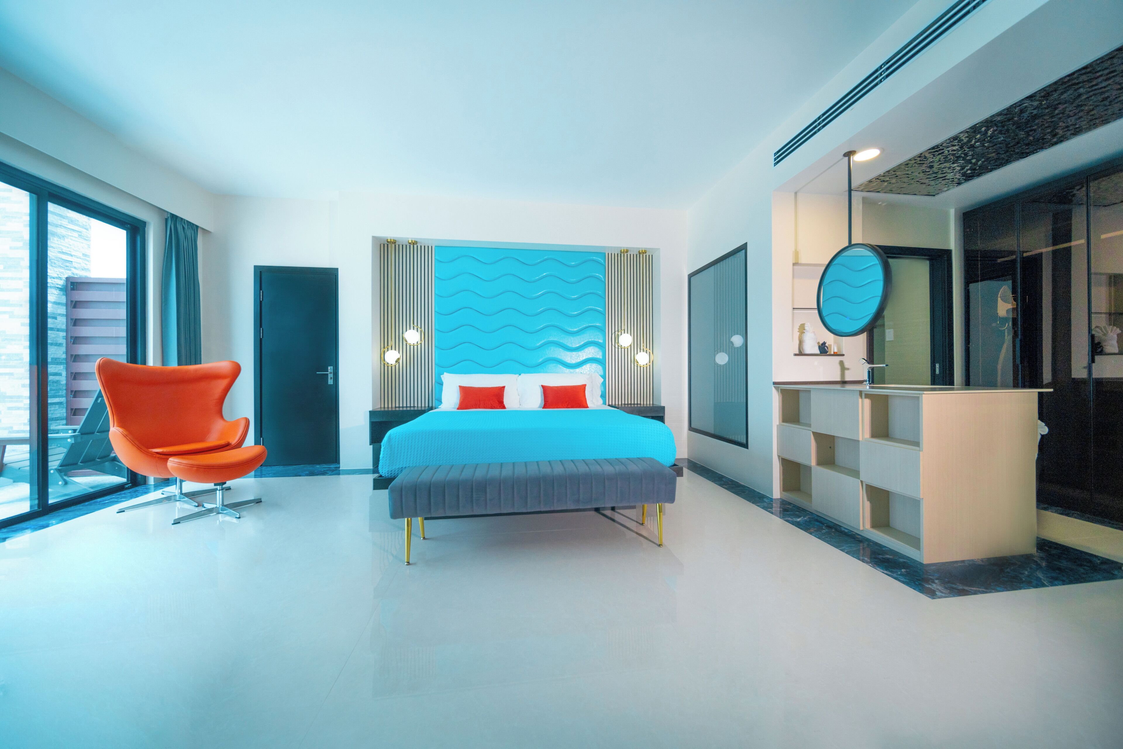 A modern hotel room with a large bed, a bright window, a seating area, and a vanity with a mirror.
